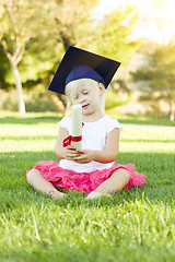 Image showing Little Girl In Grass Wearing Graduation Cap Holding Diploma With