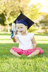 Image showing Little Girl In Grass Wearing Graduation Cap Holding Diploma With