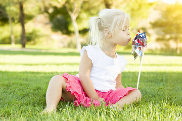Image showing Little Girl In Grass Blowing On Pinwheel
