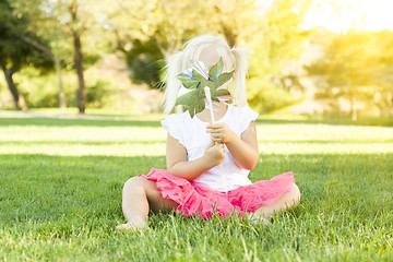 Image showing Little Girl In Grass Blowing On Pinwheel