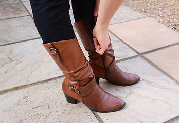 Image showing Young woman zipping up her fashionable leather boots