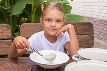 Image showing Girl with a ladle in the bowl puts porridge for breakfast