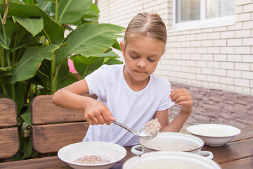 Image showing Girl with a ladle of porridge shifts the pan in a bowl