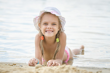 Image showing Happy little girl six years lying on the sand on the bank of the river