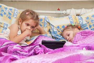 Image showing Two girls lying in bed looking at a tablet computer