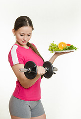 Image showing Beautiful athlete with a dumbbell in one hand and a plate of fruit in another