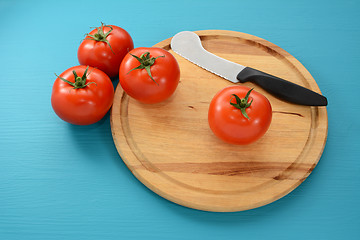 Image showing Four tomatoes on a chopping board with a knife