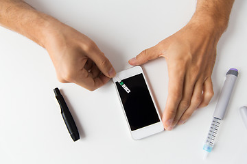 Image showing close up of man with smartphone making blood test