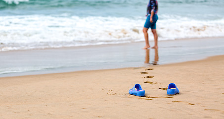 Image showing Beach Slippers and Blurred Silhouette of a Woman in Waves 