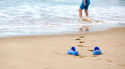 Image showing Beach Slippers and Blurred Silhouette of a Woman in Waves 