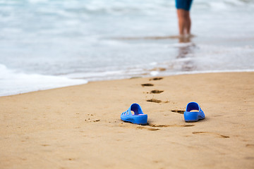 Image showing Beach Slippers and Blurred Silhouette of a Woman in Waves 