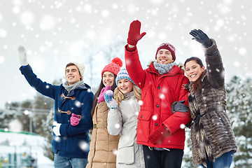 Image showing happy friends waving hands on ice rink outdoors