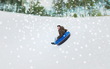 Image showing happy young man sliding down on snow tube