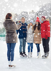 Image showing happy friends with smartphone on ice skating rink