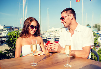 Image showing smiling couple with champagne and gift at cafe