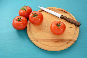 Image showing Tomatoes with a serrated knife on a wooden board