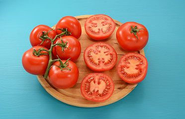 Image showing Tomatoes - on the vine, halved and whole on a wooden board