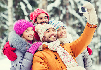 Image showing smiling friends with camera in winter forest