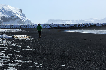 Image showing Woman walks along black sand beach in Vik, Iceland