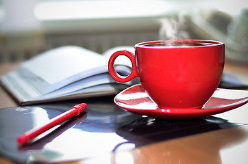 Image showing Red cup of hot coffee, notepad and pencil on the desktop in the 