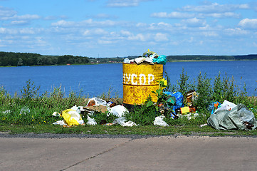 Image showing Overflowing barrel with rubbish and waste disposal on the waterf