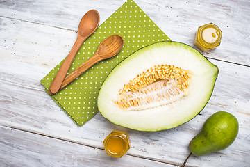 Image showing Cut melon with honey and green pear on wood