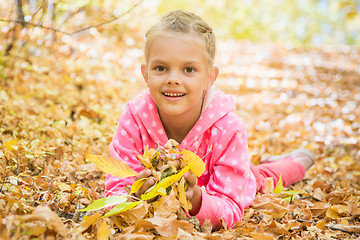 Image showing Six year old girl lying on the yellow fallen leaves