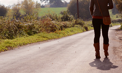 Image showing Young woman walks up a country lane alone