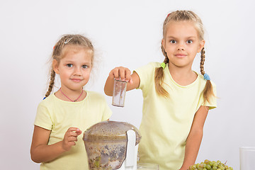 Image showing Two girls looking to frame squeezing fruit juice in a juicer