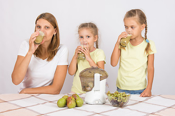 Image showing Mother and two daughters drink freshly juice from the pears and grapes