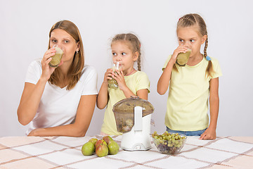 Image showing Mother and two daughters taste the freshly prepared juice from pears and grapes