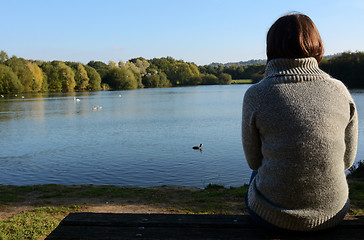 Image showing Woman in a warm jumper sitting alone by a lake