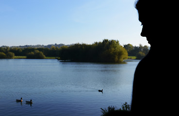 Image showing Woman in silhouette sits beside a lake