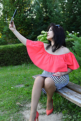 Image showing Brunette girl sitting on a bench in the park with tablet