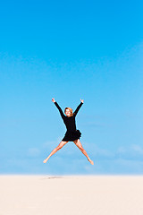 Image showing Girl jumping in the air on sand dune.