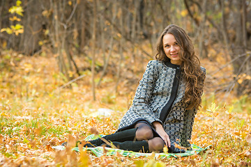 Image showing Young beautiful girl in a yellow coat sitting on fallen leaves in the forest