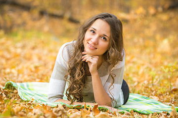 Image showing Young beautiful girl lying on a rug in the autumn forest