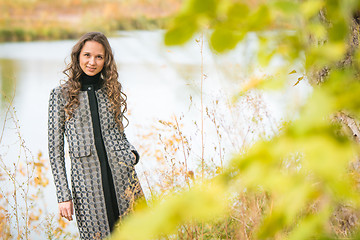 Image showing Portrait of a young girl on the background of autumn river with blurred leaves in the foreground