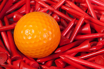 Image showing Orange golf ball lying between wooden tees