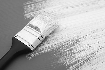 Image showing Dirty paintbrush with white paint on half-painted board