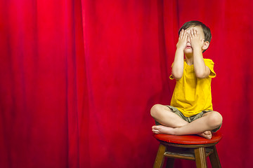 Image showing Boy Covering Eyes Sitting on Stool in Front of Curtain