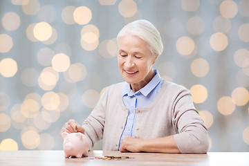 Image showing senior woman putting money to piggy bank