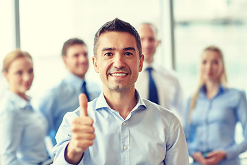 Image showing smiling business team showing thumbs up in office