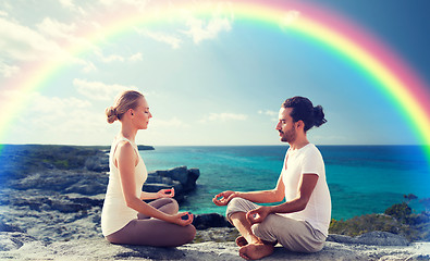 Image showing happy couple meditating in lotus pose on beach