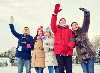 Image showing happy friends waving hands on ice rink outdoors