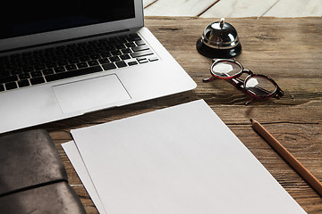 Image showing The laptop, blank paper, glasses and small bell on the wooden table 