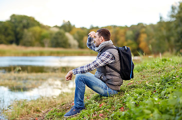 Image showing smiling man with backpack resting on river bank