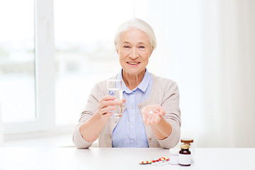 Image showing happy senior woman with water and medicine at home