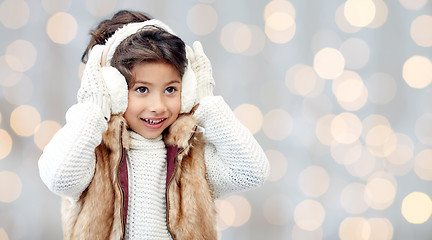 Image showing happy little girl in earmuffs over holidays lights