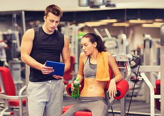 Image showing smiling young woman with personal trainer in gym